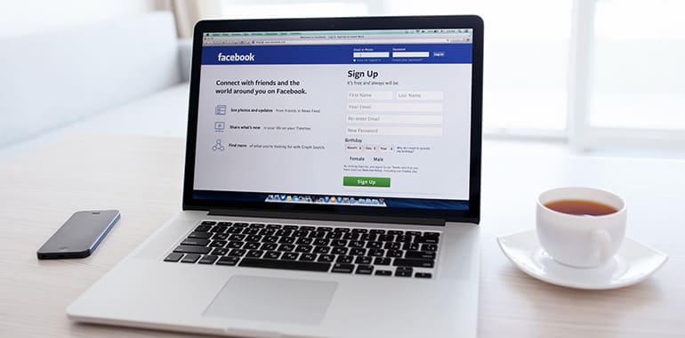 Laptop showing Facebook login page. Tea and phone placed to either side